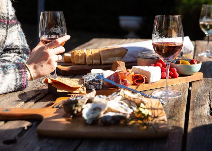 Selection of cheeses on board with wine glasses on table at Shut The Gate Snowy Mountains Cellar Door in Berridale, Jindabyne 